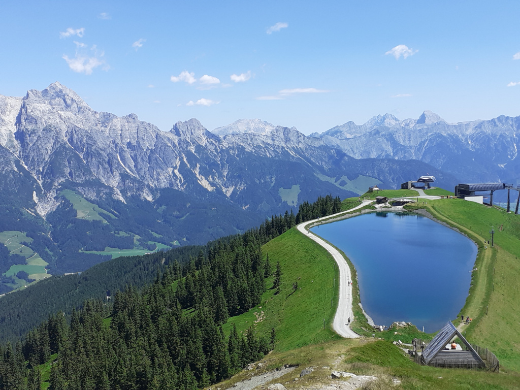 Berglandschaft mit Speicherteich, Wanderweg und Bergstation auf einem grünen Höhenrücken