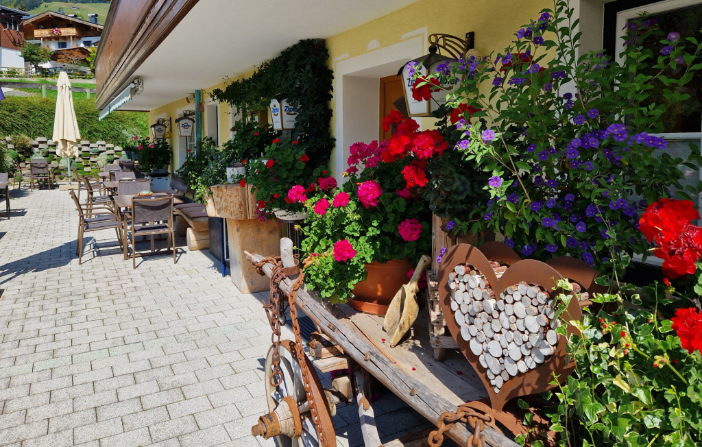 blumengeschmückte Terrasse mit Tischen und Stühlen vor einem gelben Gebäude
