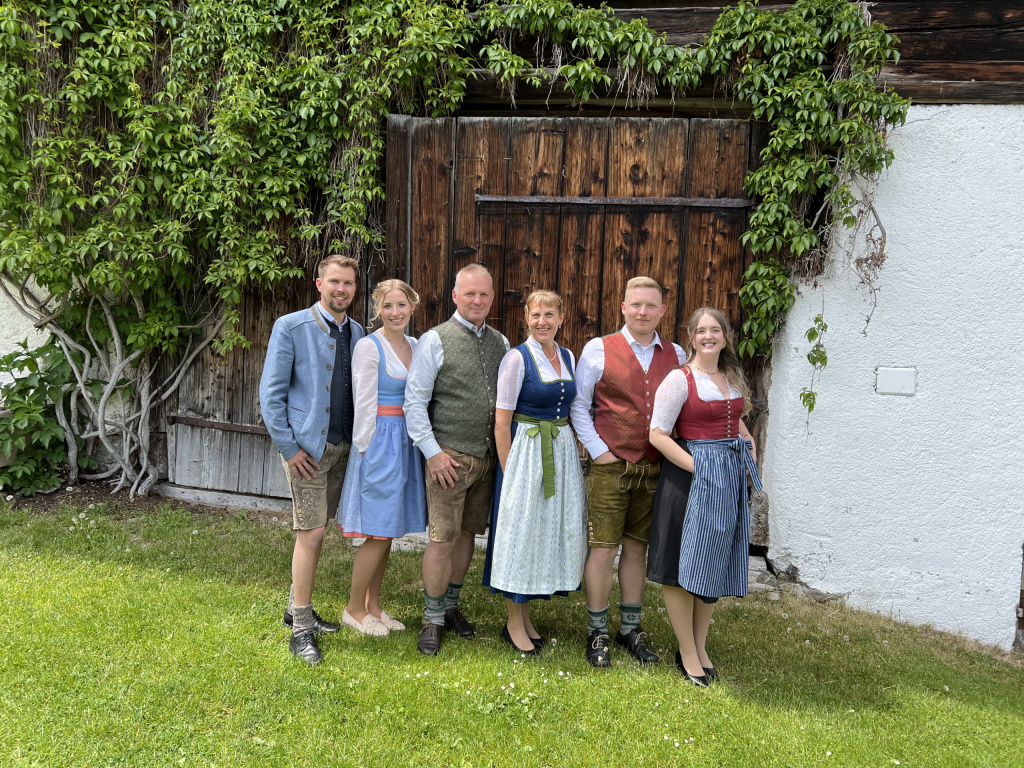 Gruppe in Tracht vor hölzerner Scheunentür mit Bewuchs